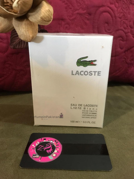 Lacoste Eau de Lacoste L.12.12 Blanc Eau de Toilette 100ml perfume box displayed with decorative wooden flowers and PerfumeinPakistan branding card