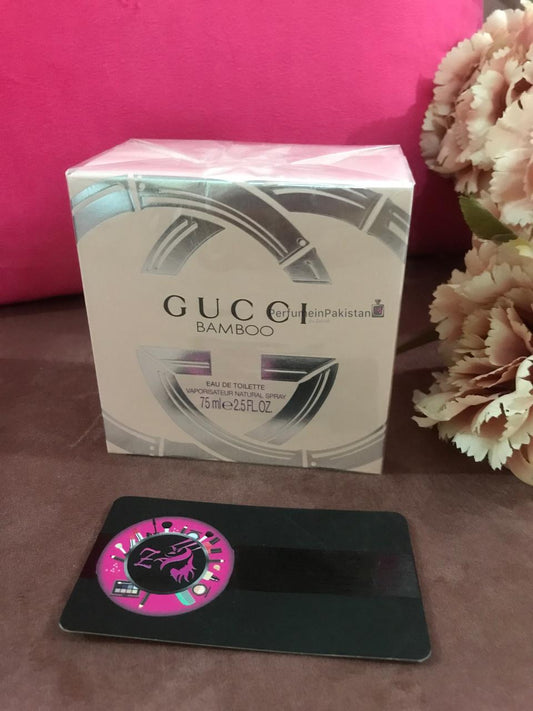 Gucci Bamboo Eau de Toilette 75ml perfume box displayed on a brown surface with floral decoration and PerfumeinPakistan branding card
