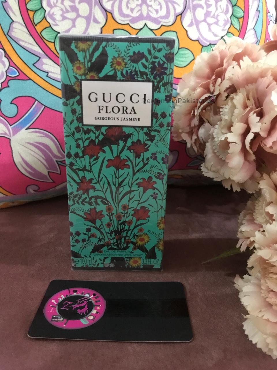 Gucci Flora Gorgeous Jasmine Eau de Parfum 100ml perfume box with floral design displayed beside decorative flowers and PerfumeinPakistan branding card