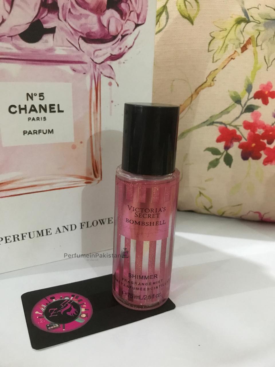Victoria's Secret Bombshell Shimmer Fragrance Mist 75ml bottle with pink shimmer formula displayed against a floral background.