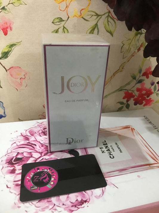 Dior Joy Eau de Parfum 100ml perfume box displayed on a floral-themed background with PerfumeinPakistan branding card
