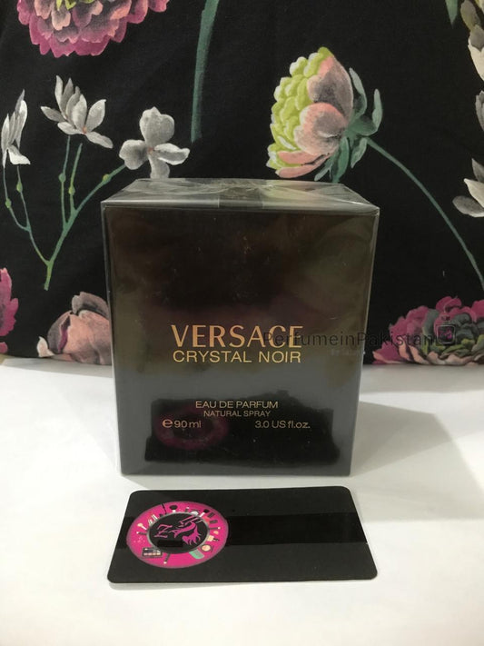 Versace Crystal Noir Eau de Parfum 90ml perfume box displayed against a floral backdrop with PerfumeinPakistan branding card
