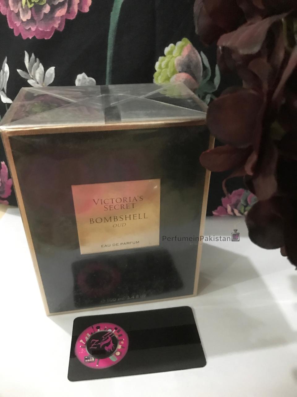 Victoria's Secret Bombshell Oud Eau de Parfum 100ml perfume box displayed against a floral backdrop with PerfumeinPakistan branding card