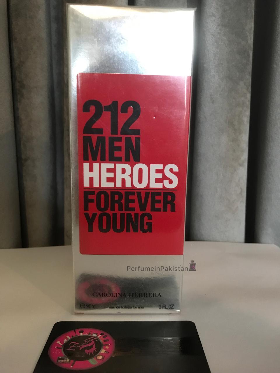 212 Men Heroes Forever Young by Carolina Herrera Eau de Toilette 90ml perfume box displayed with PerfumeinPakistan branding card on a white surface against a gray curtain background.

