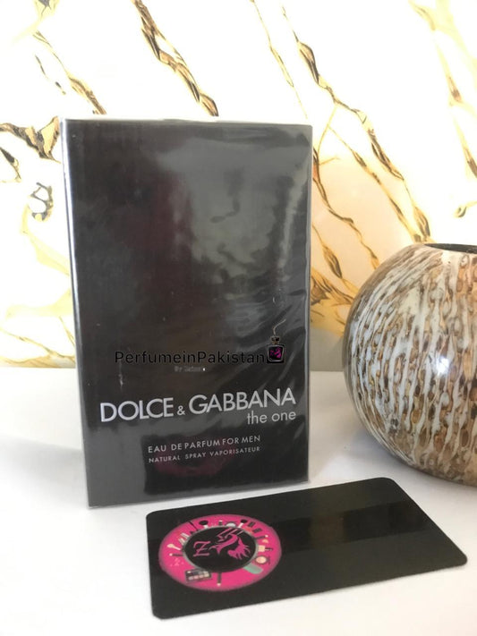 Dolce & Gabbana The One Eau de Parfum For Men 100ml perfume box displayed beside a decorative ceramic vase on a white surface with marble-pattern background and PerfumeinPakistan branding.